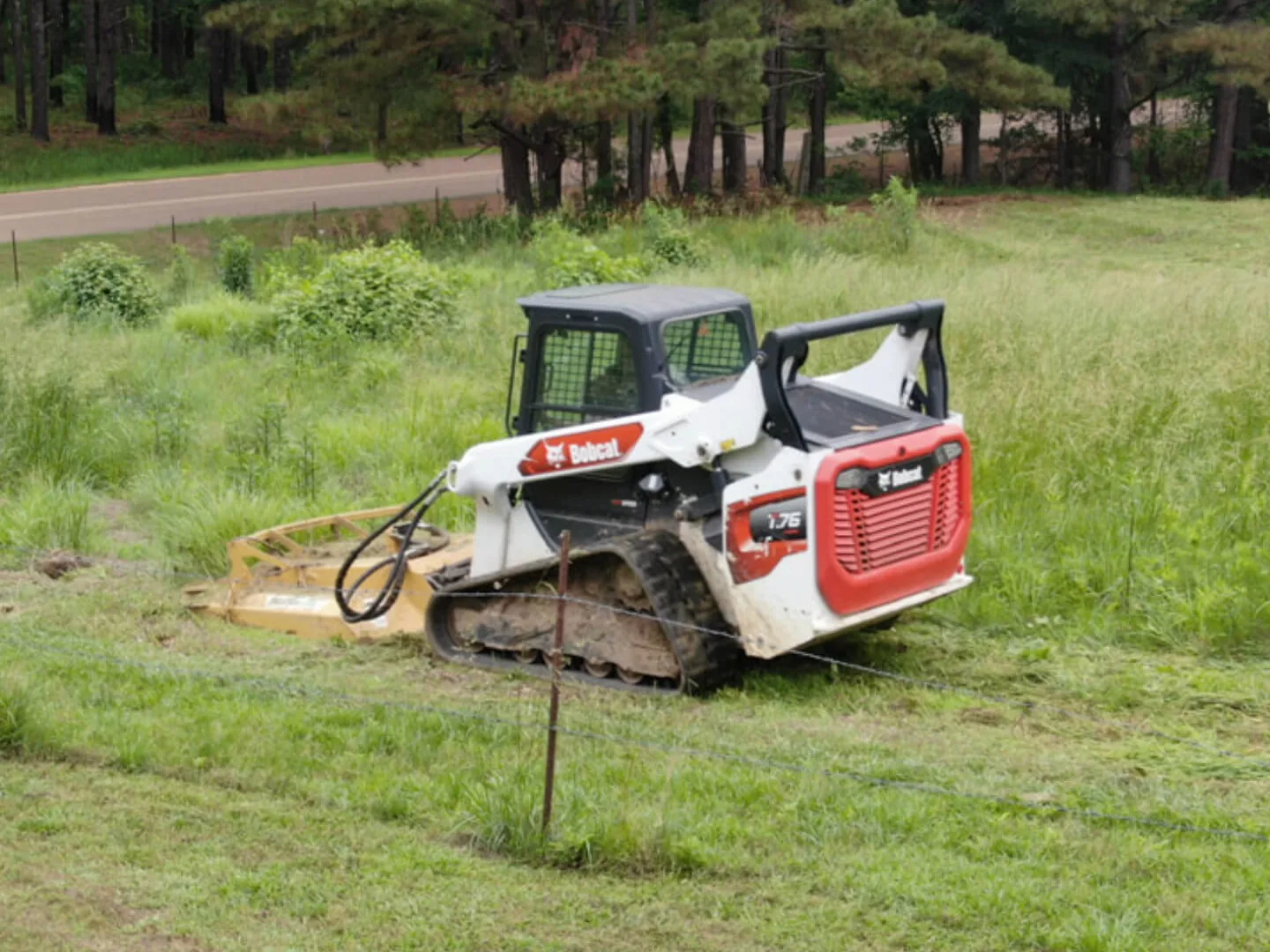 Brush hogging a tall grass pasture along a fence row with a compact track loader