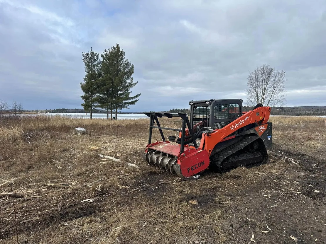 Forestry mulching head on a compact track loader beside cleared brush near the water