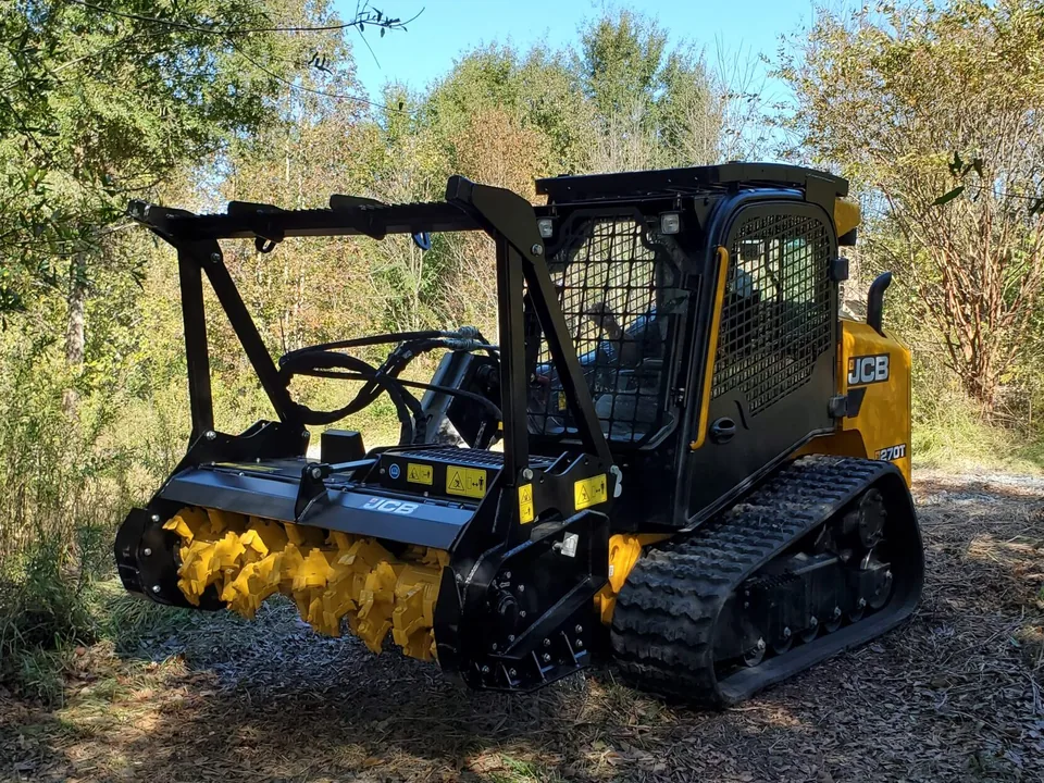 Forestry mulching head on a compact track loader parked in brushy woods
