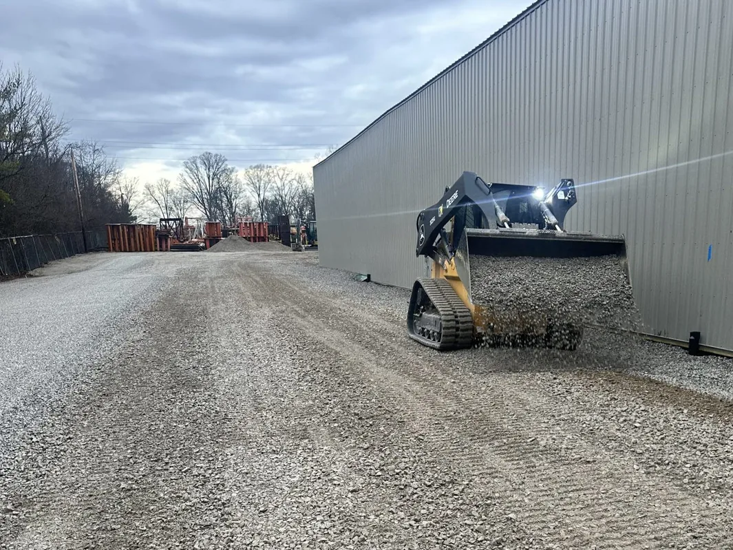 Compact track loader spreading gravel along a pole building