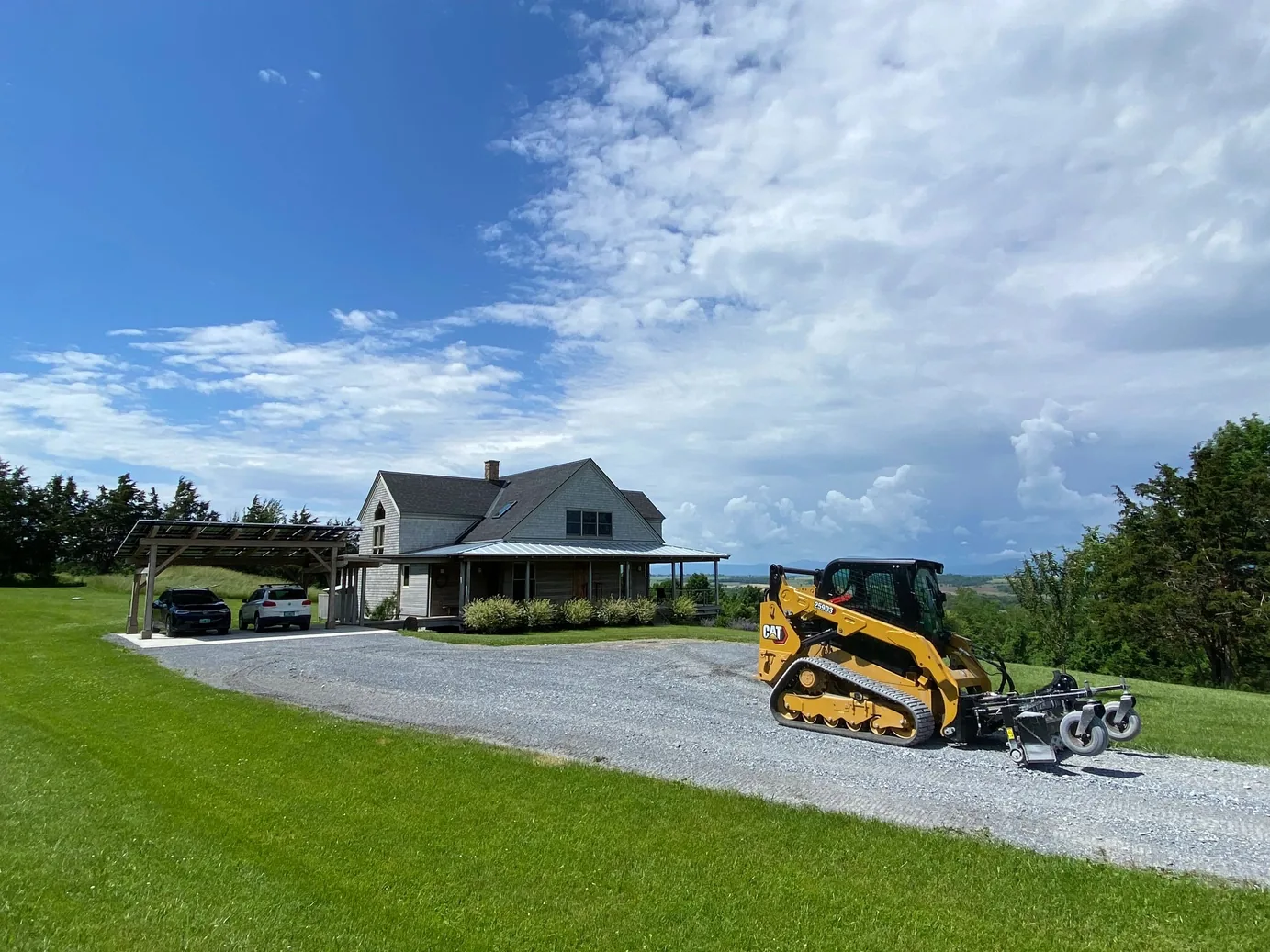 Gravel driveways: a landscape rake on a compact track loader grading a new drive beside a farmhouse