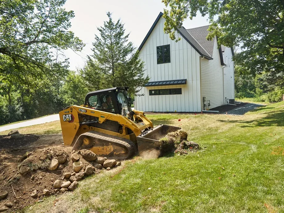 Compact track loader grading soil and rock beside a new house