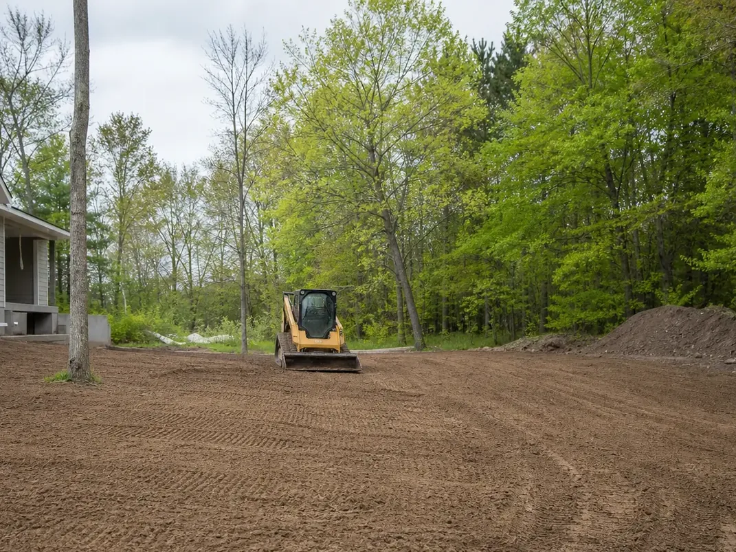 Land grading a yard beside a house with a compact track loader