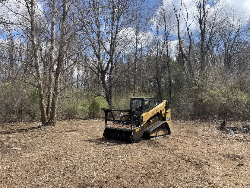 Site preparation with a compact track loader and mulching head on a cleared building site in the woods