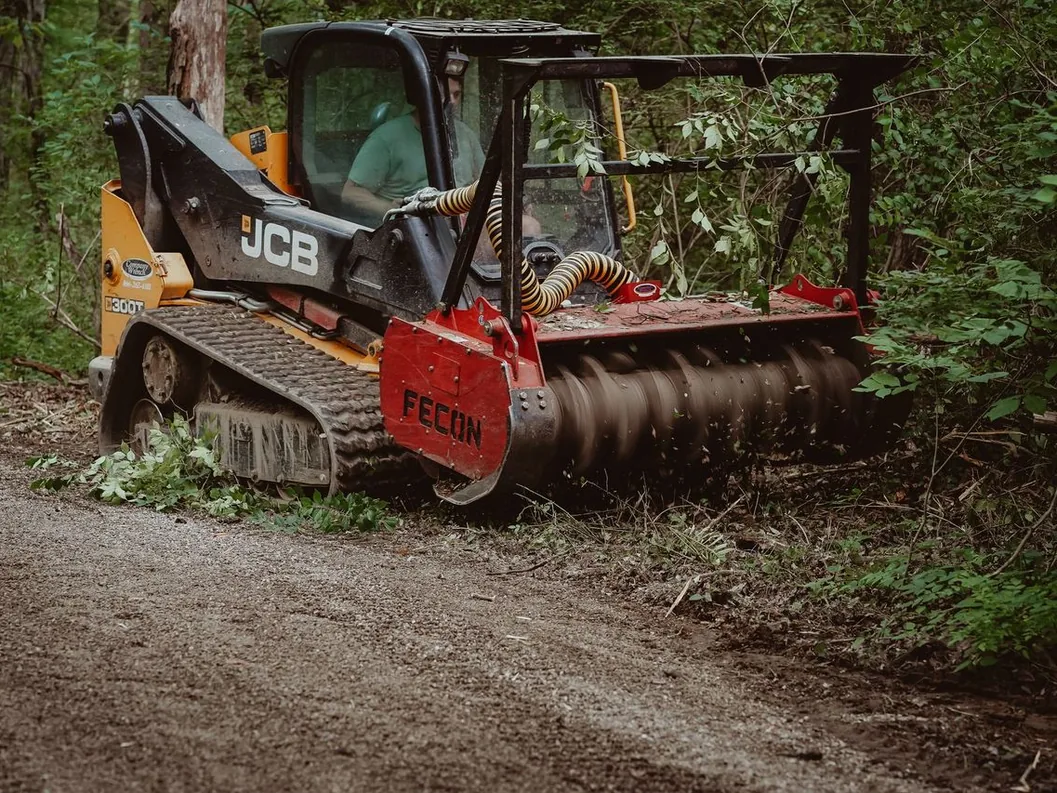 Trail clearing along a dirt lane with a mulching head cutting back brush